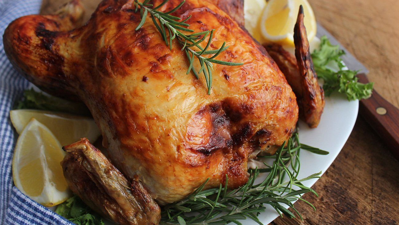 A roasted chicken on a white plate with lemons and herbs.