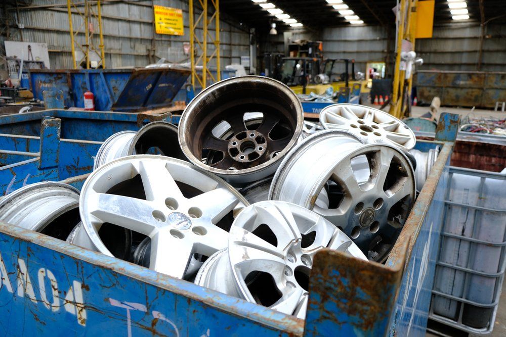 Une benne bleue déborde de jantes de voiture dans un centre de recyclage.
