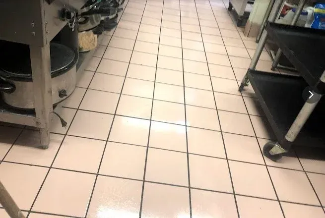 A kitchen floor with pink tiles and black grout, visible from a low angle.