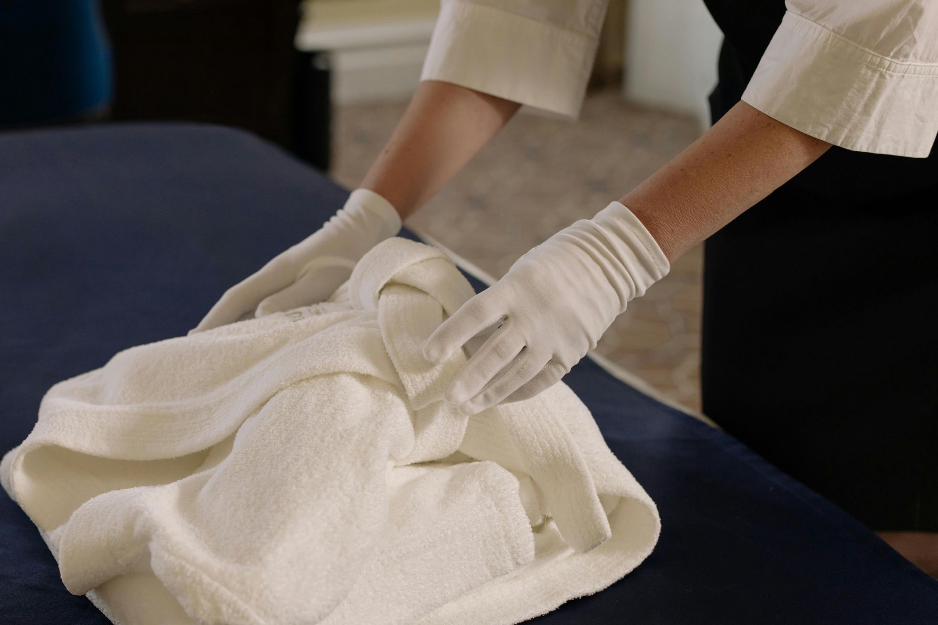 Person in white gloves folding a white towel on a blue surface.