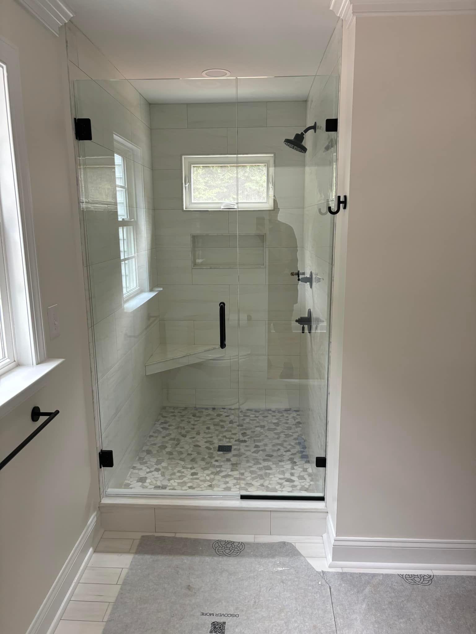 Modern bathroom shower with glass enclosure, white tile walls, and pebble-pattern floor.