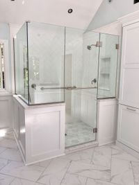 Corner glass shower with black frame in a beige bathroom, beside a white sink and patterned rug