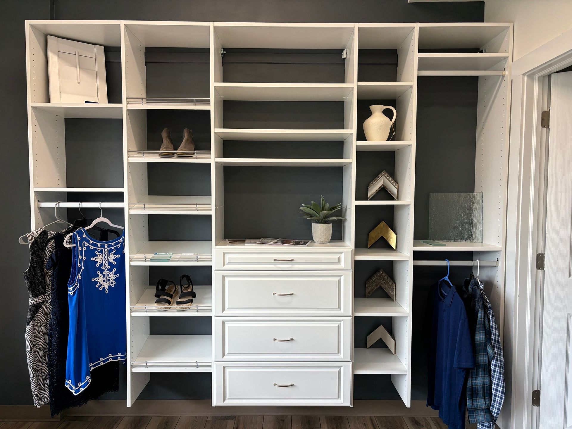 Custom closet with white shelving, drawers, and hanging clothes in a bedroom.