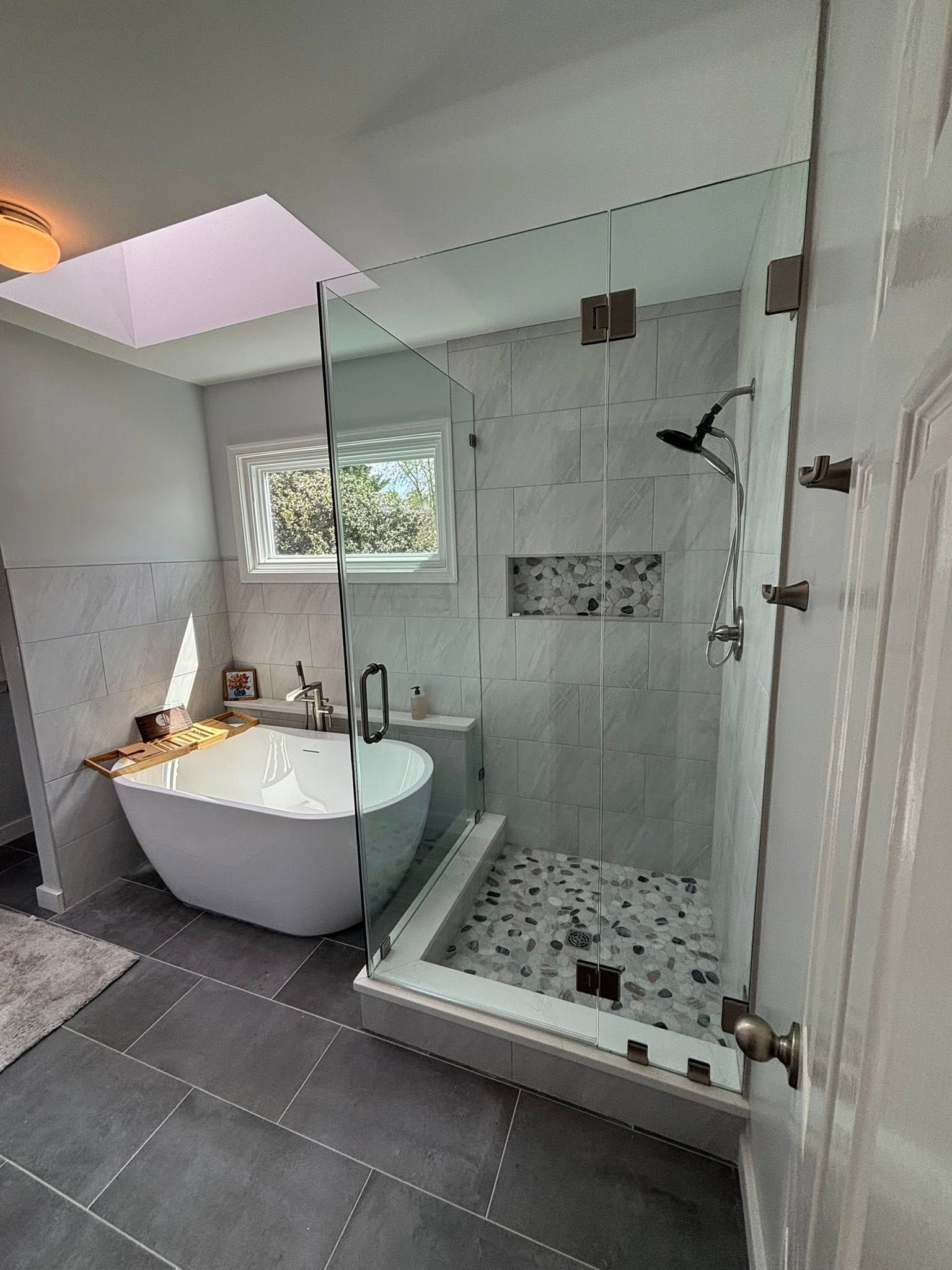 Modern bathroom with a freestanding tub, glass shower, gray tile floor, and skylight.