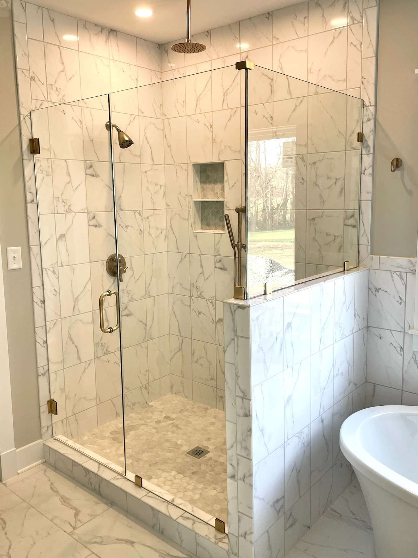 Glass-enclosed walk-in shower with marble tile, bench, and rainfall showerhead in a bright bathroom