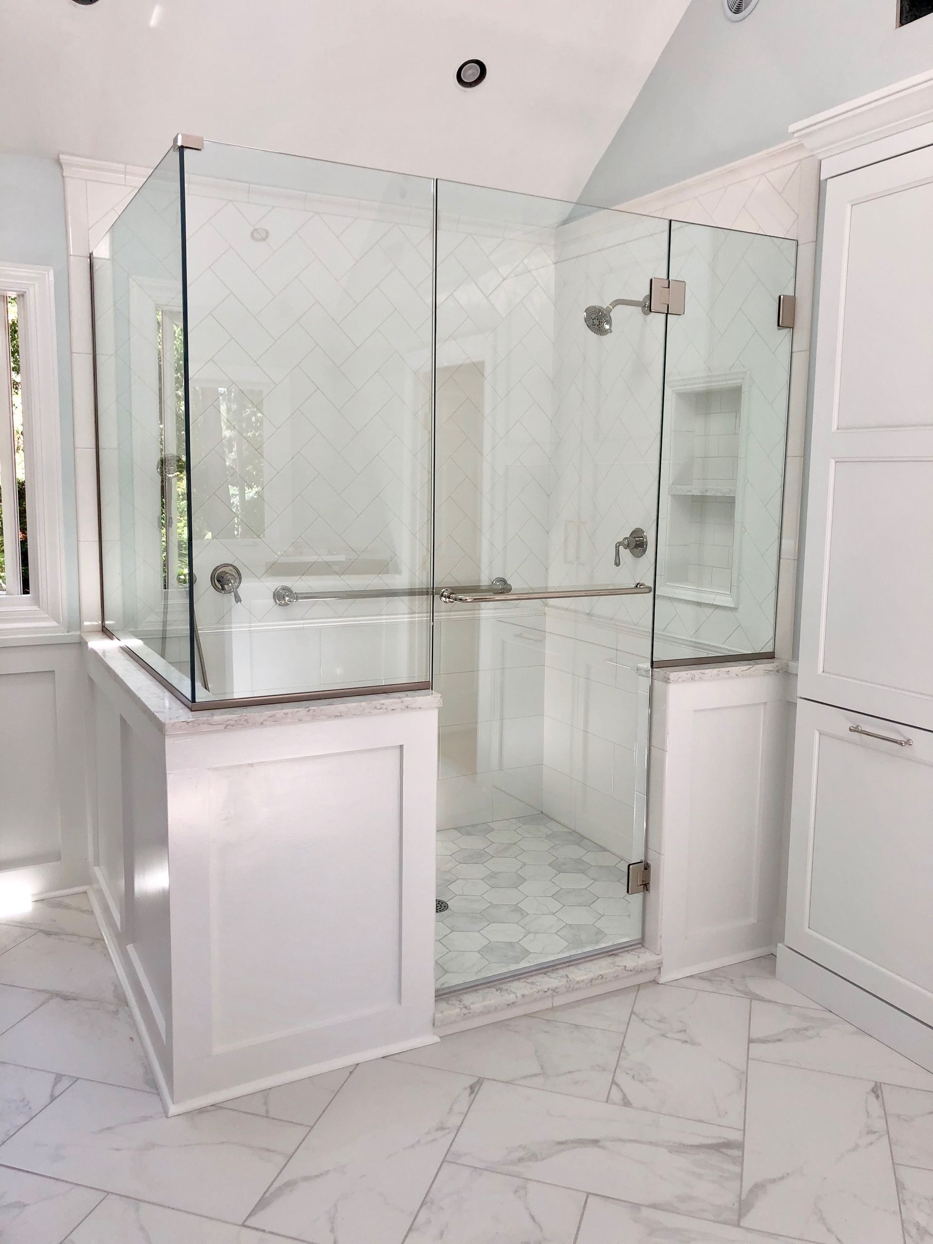 Bright white bathroom with glass shower enclosure, double sink vanity, and marble-pattern tile floor.