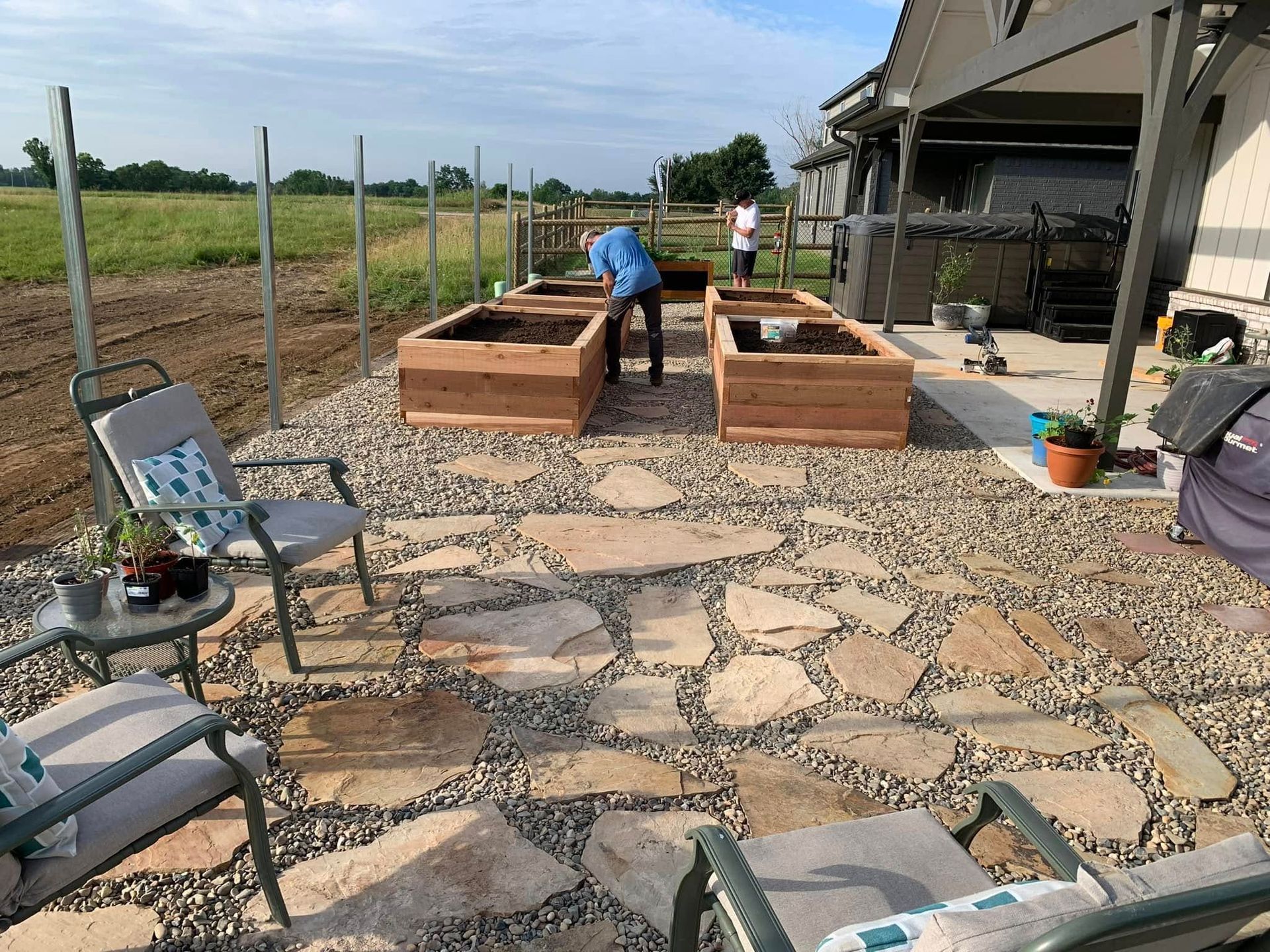 A backyard garden with raised beds, flagstone patio, and two people gardening.