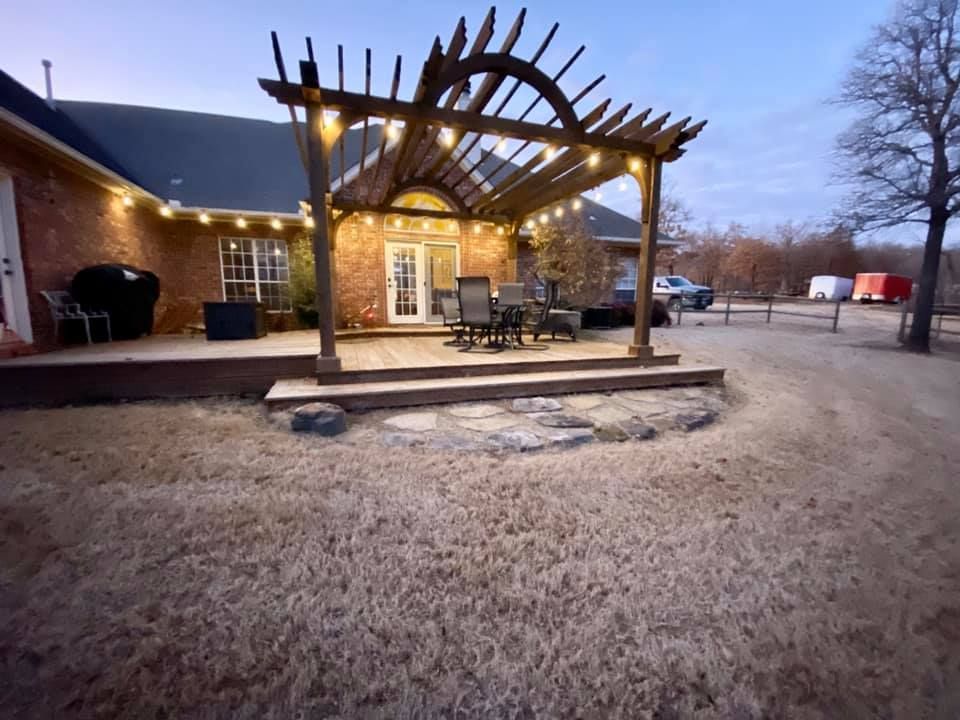 Wooden pergola with string lights over a patio, brick house in the background.