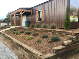 Brown building with a wooden porch and flower beds, pathway.