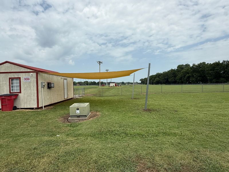 A small wooden building and a yellow shade canopy sit on a grassy field under a cloudy sky.