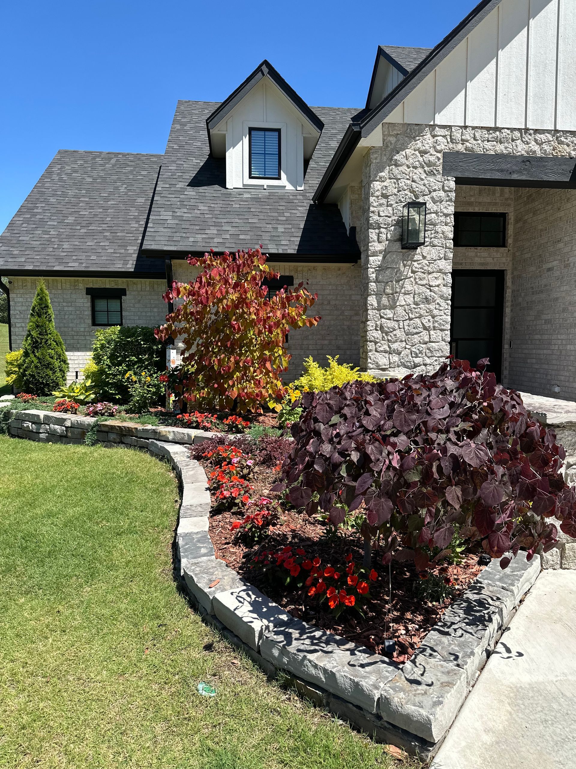 Brown building with a wooden porch and flower beds, pathway.