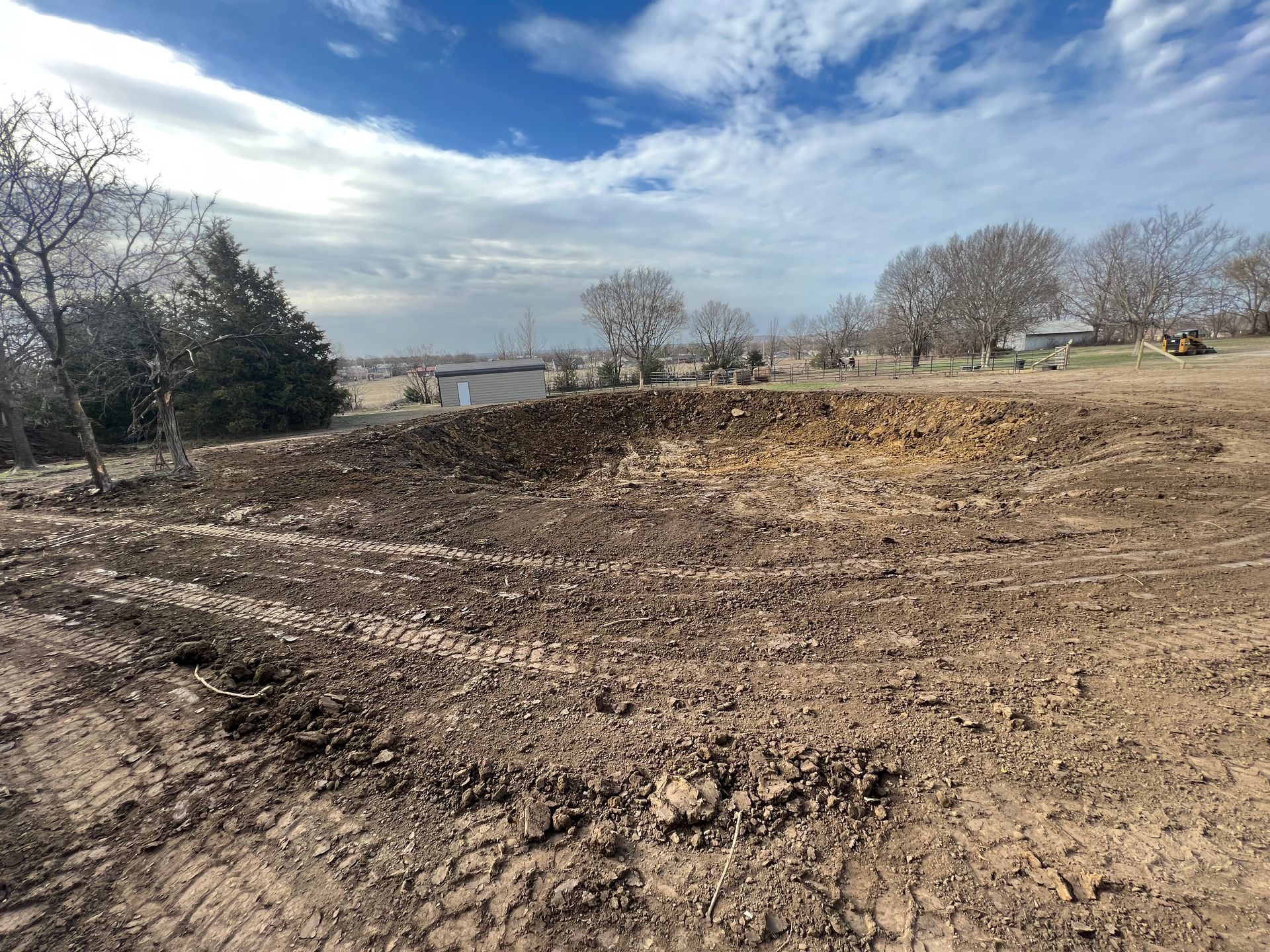 A pond surrounded by bare trees and snowy ground, seen from a car window on a cloudy day.