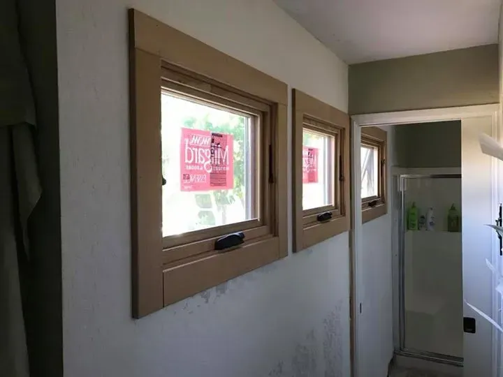 Two tan-framed windows on a light wall, next to a doorway. Bathroom partially visible through the doorway.