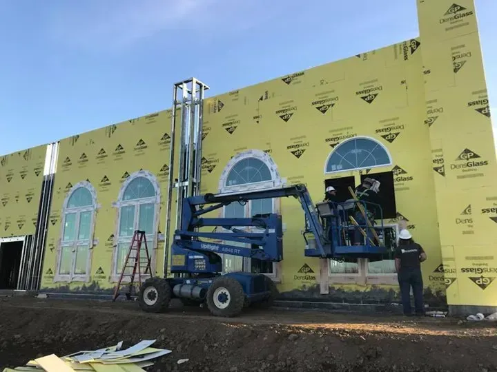 Workers on lift installing window on building exterior; blue lift, yellow wall covering.