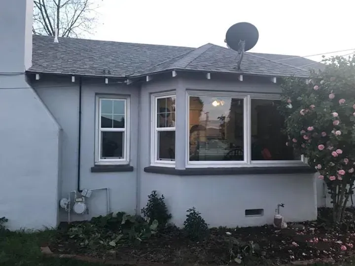 Light blue house with white-framed windows, bay window, and satellite dish. A rose bush blooms.