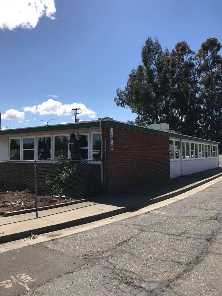 School building with a brown wooden side and a white-framed windowed section, set on a sunny day.