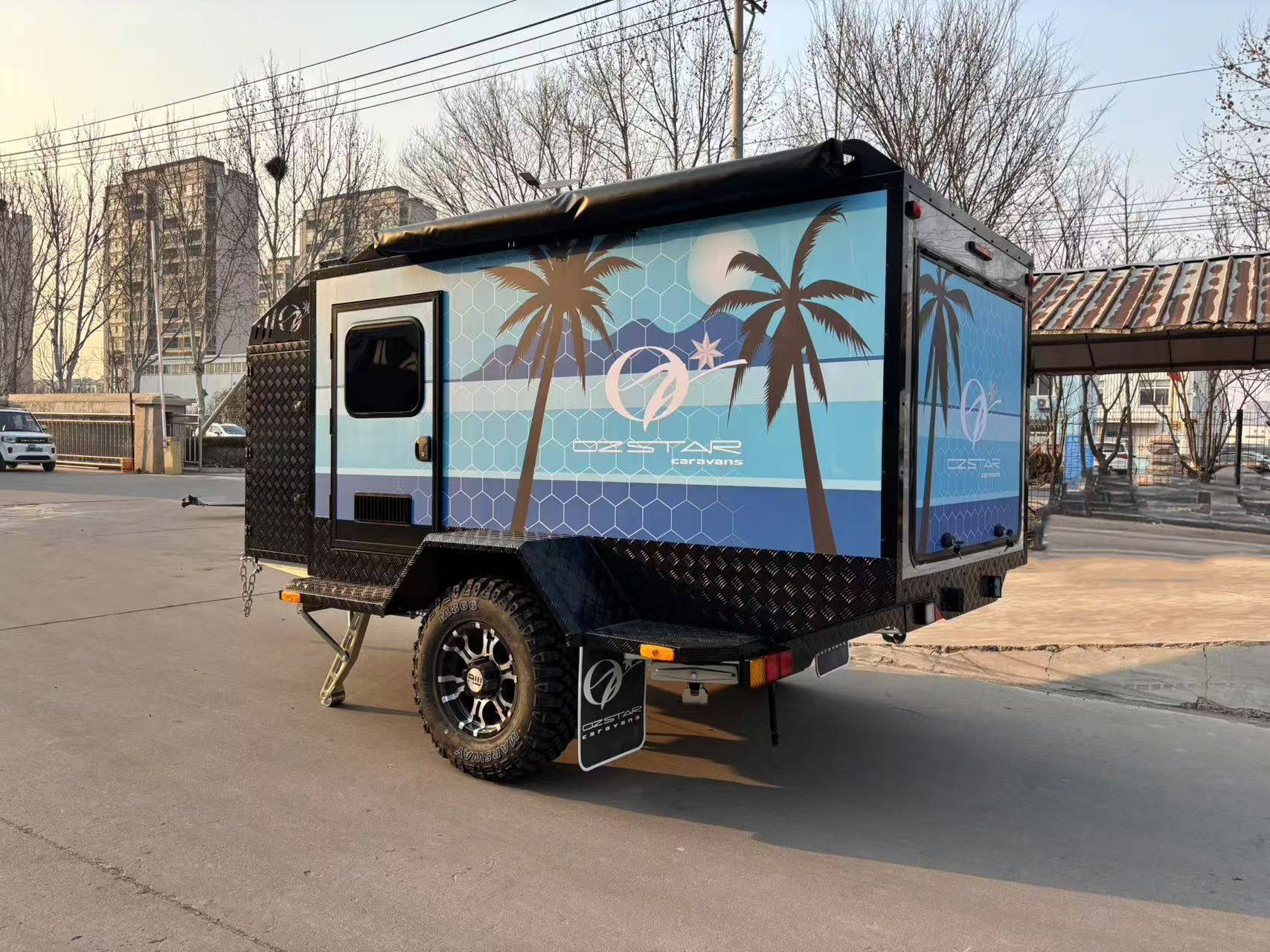 A blue 7-foot caravan trailer with palm trees on the side is parked on the side of the road.