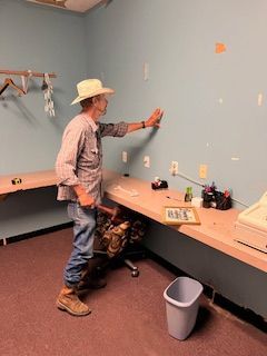 A man in a cowboy hat is measuring a wall in a room.