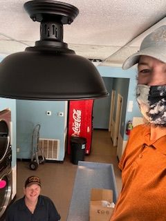 A man wearing a mask is standing next to another man in a laundromat.