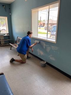A man is kneeling down in a room painting a wall.