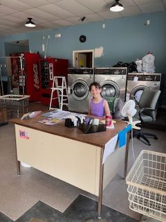 A girl is sitting at a desk in a laundromat.