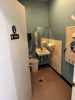 A bathroom with a sink , mirror and trash can.