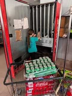 A little girl is standing in front of a coca cola vending machine.