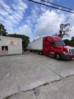 A red semi truck with a white trailer is parked in front of a building.
