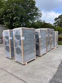 A row of washing machines are wrapped in plastic and sitting on wooden pallets.