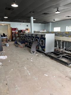 A man is working on a row of washing machines in a laundromat.
