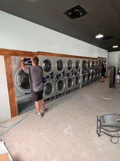 A man is standing in front of a row of washing machines in a laundromat.