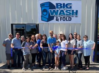 A group of people are standing in front of a big wash and fold sign.