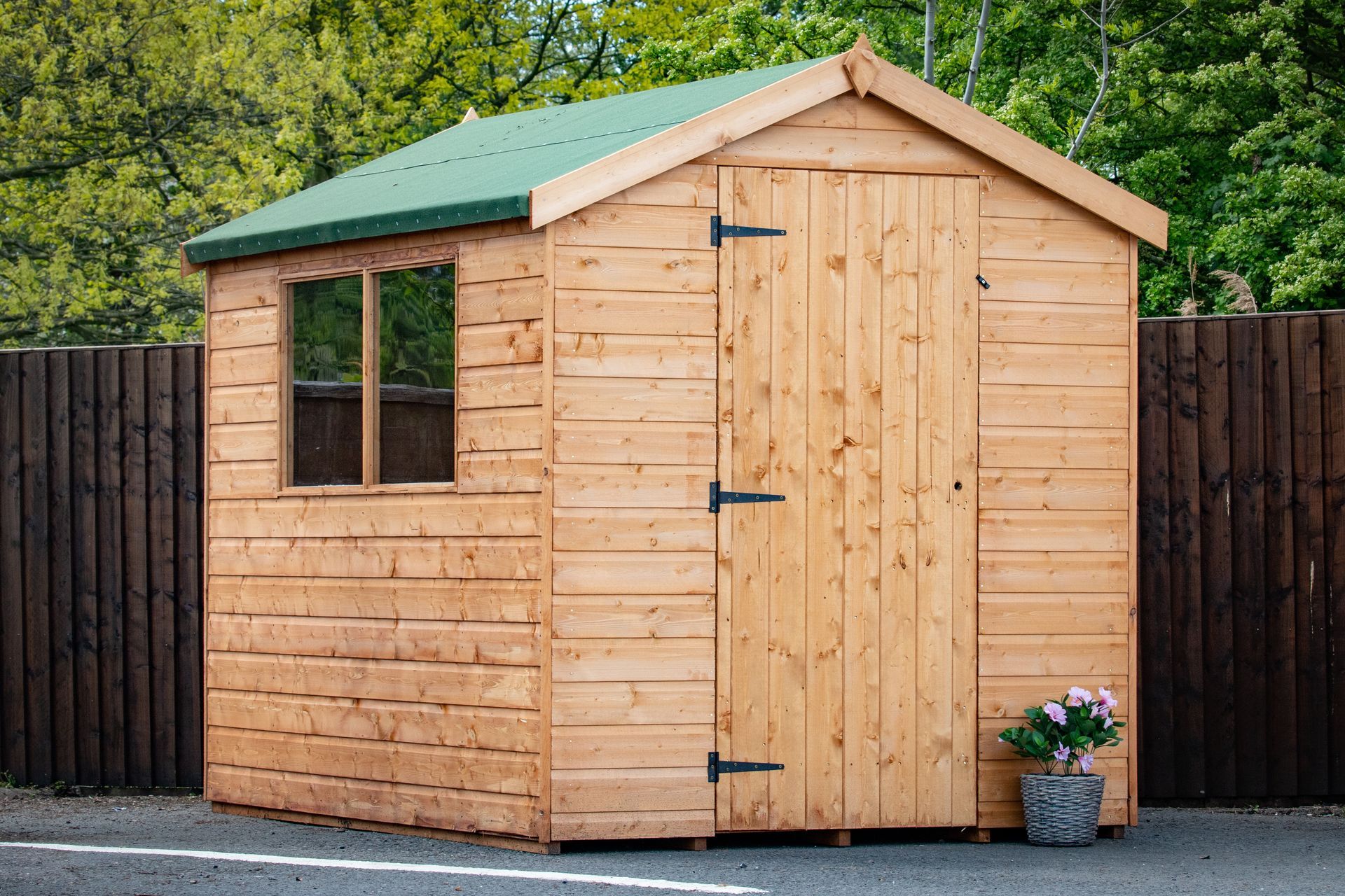 A wooden shed with a green roof is sitting next to a fence.