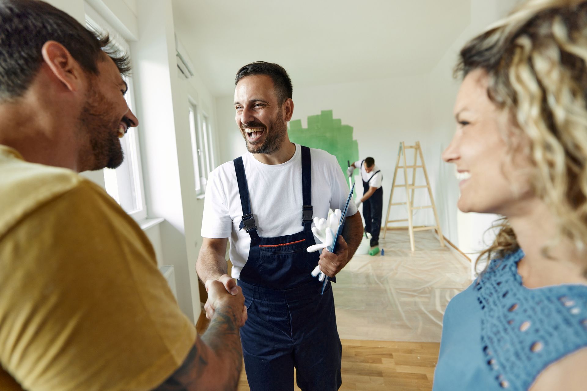 Painter shaking hands with client in a room being renovated.