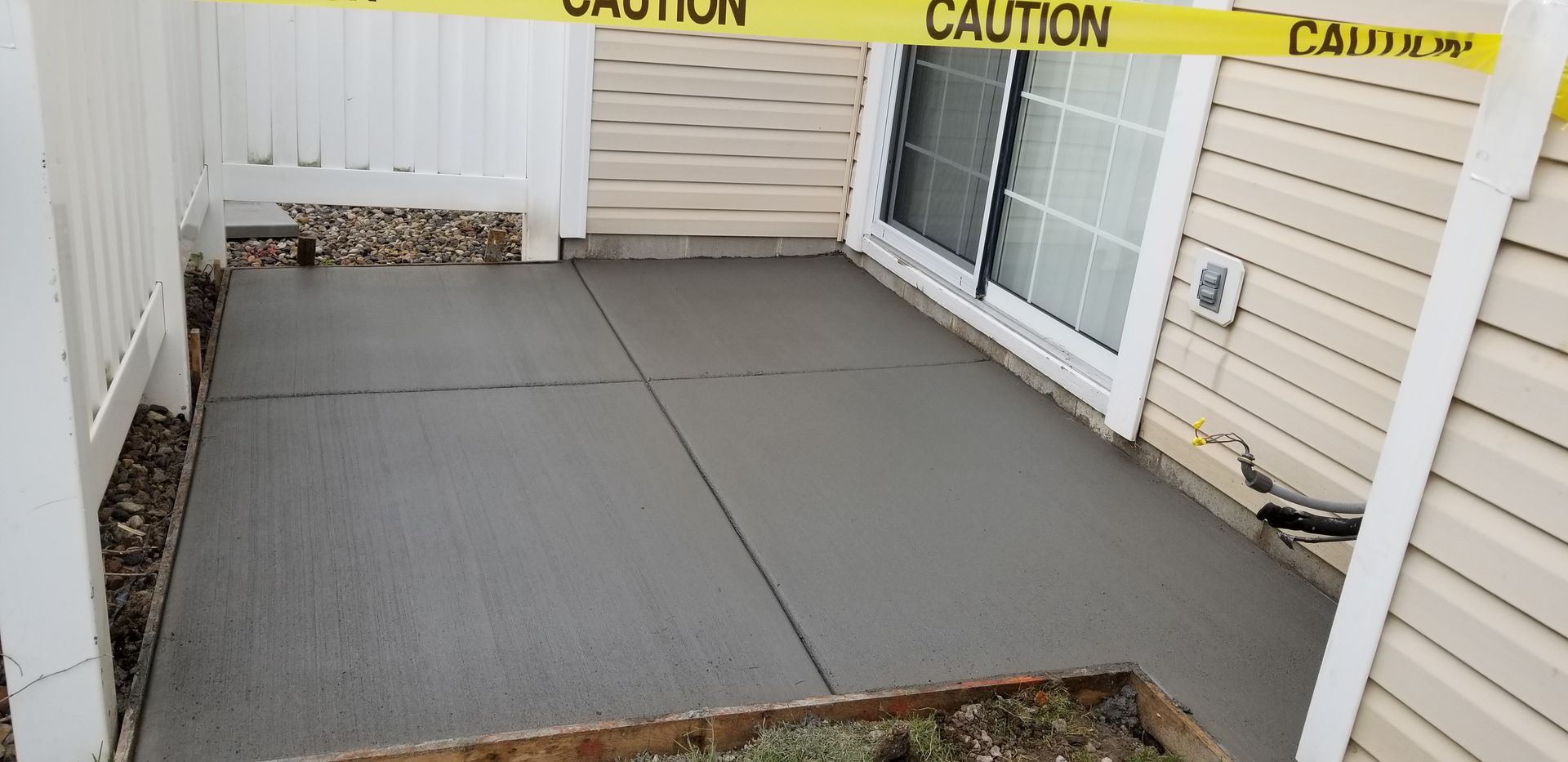 Newly poured concrete patio, yellow caution tape overhead.