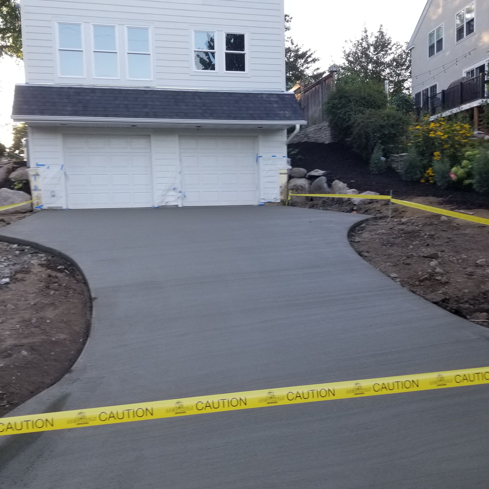 Newly poured concrete driveway in front of a white house with a two-car garage. Yellow caution tape.