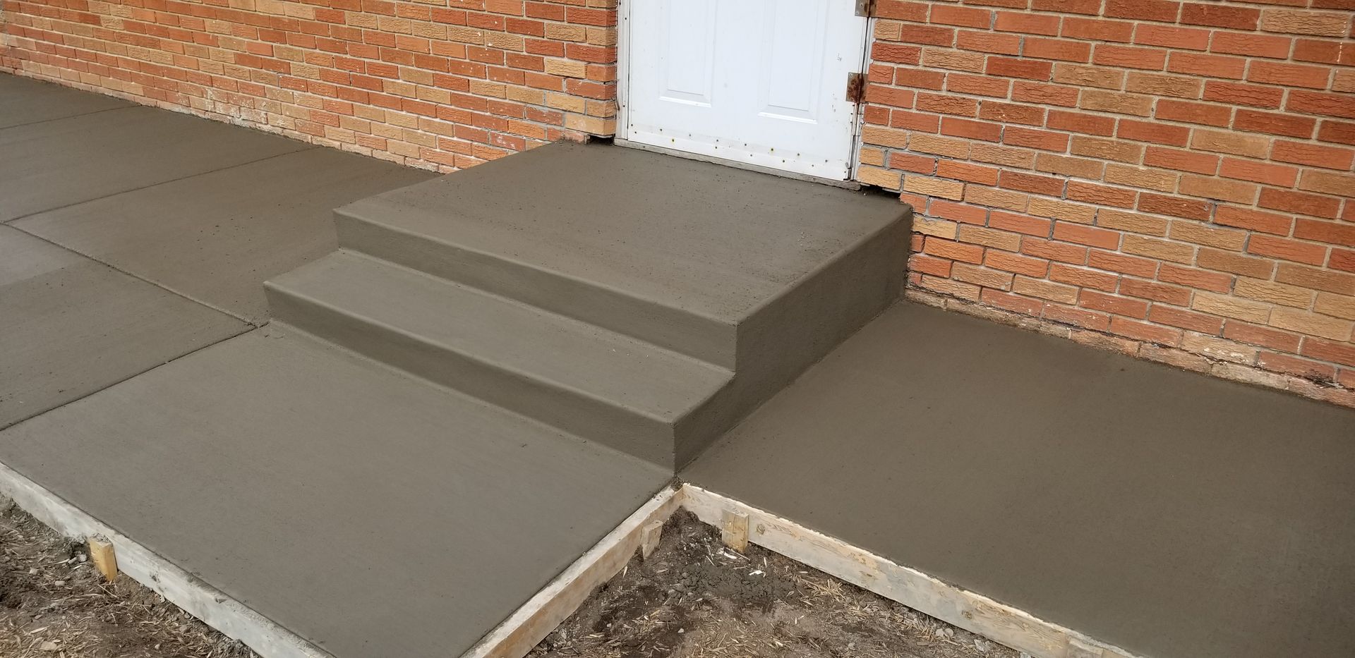 Newly poured concrete steps and walkway next to a brick building.