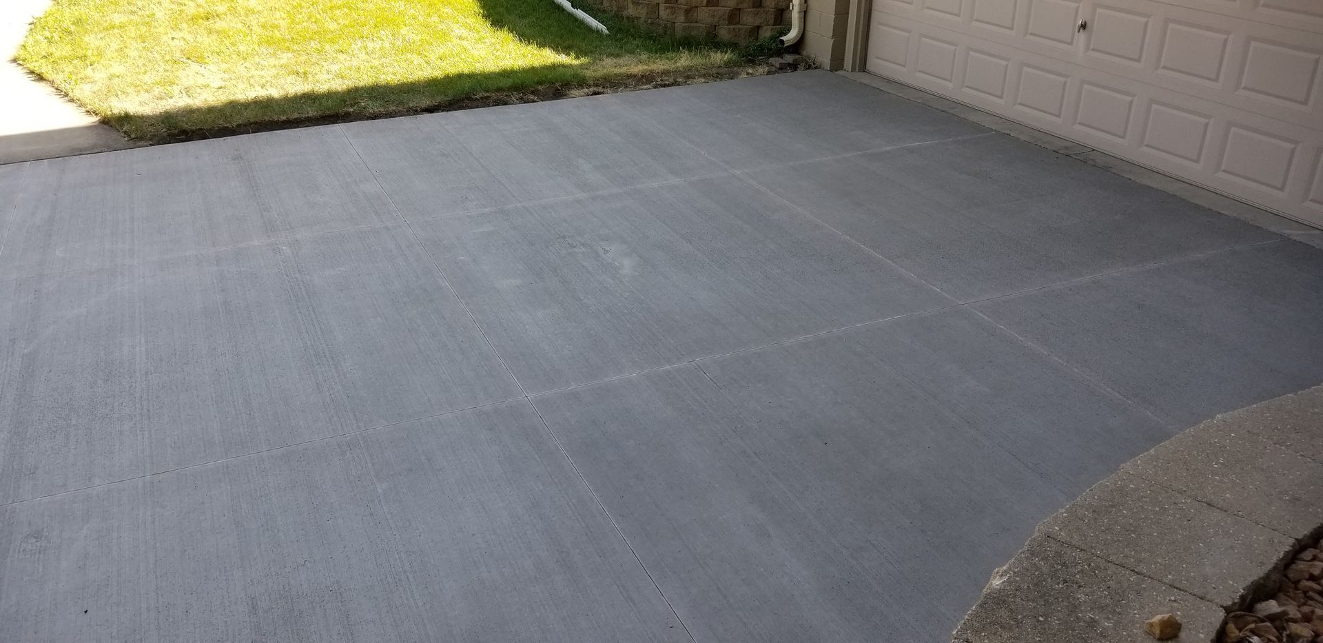 A gray concrete patio next to a grassy area and a beige building.