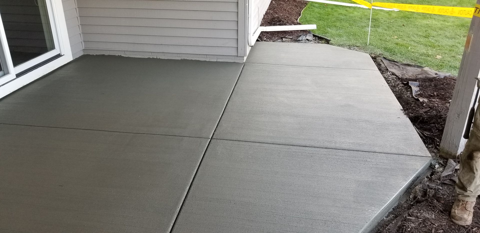 Newly poured concrete patio next to a house with a sliding glass door and a grassy yard.