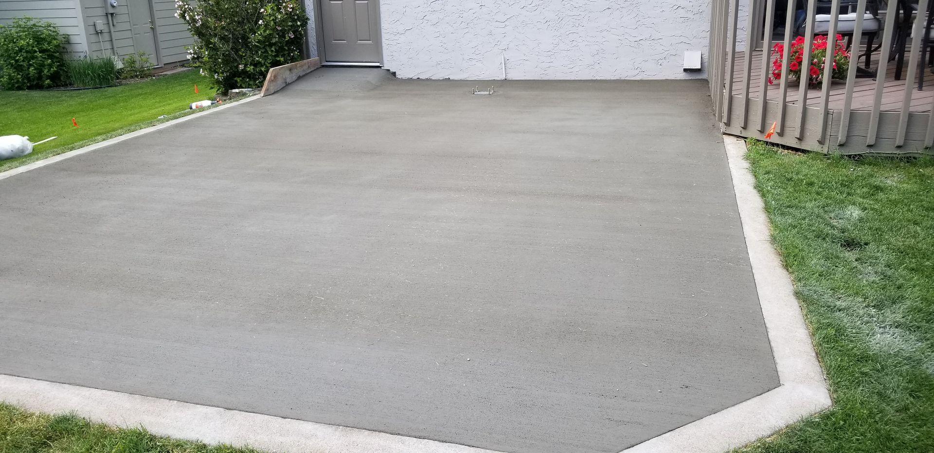 Newly poured concrete patio next to a grass lawn and deck.