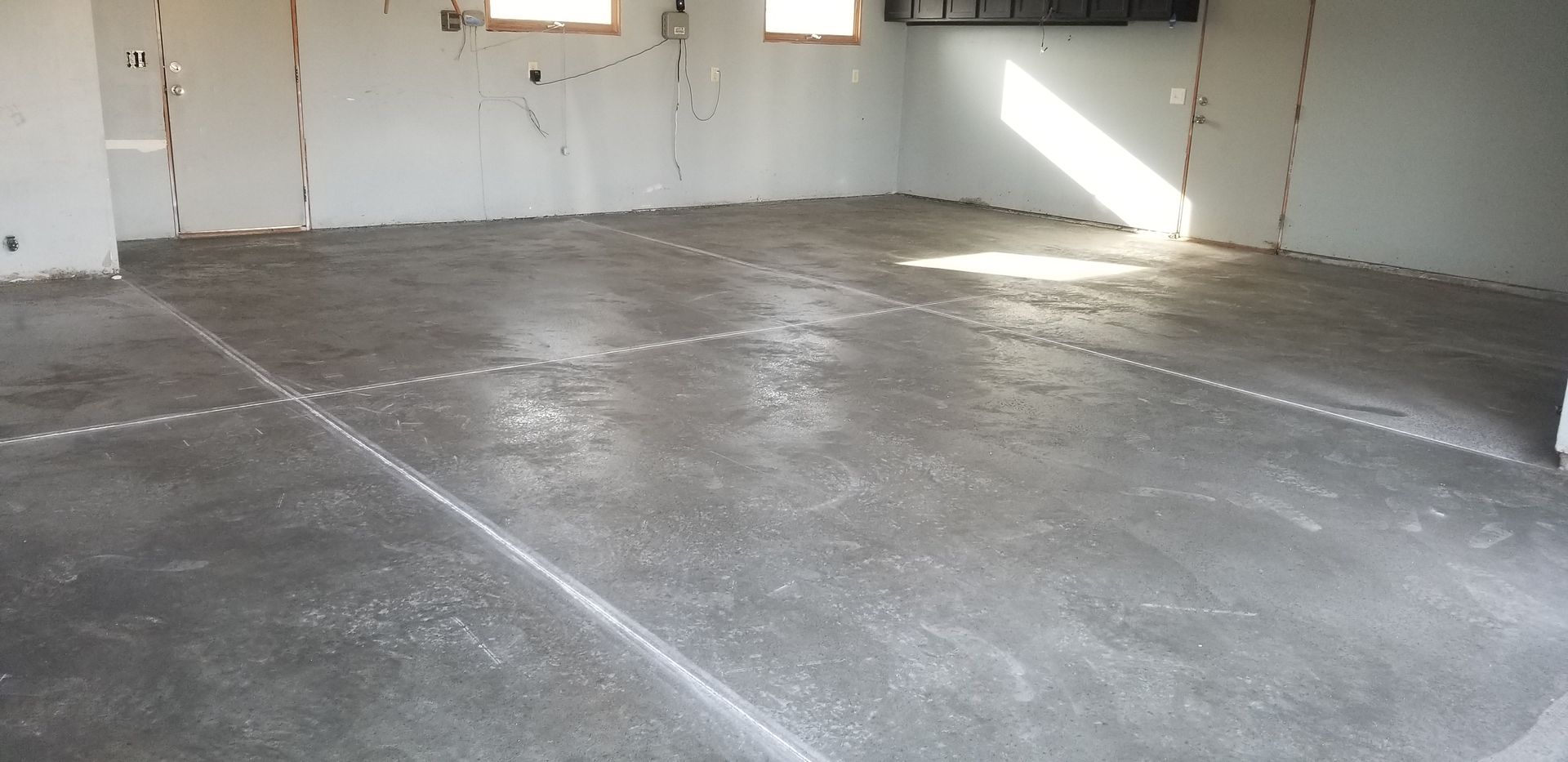 A concrete floor in a room. Walls are gray, unfinished. Sunbeam on the floor.