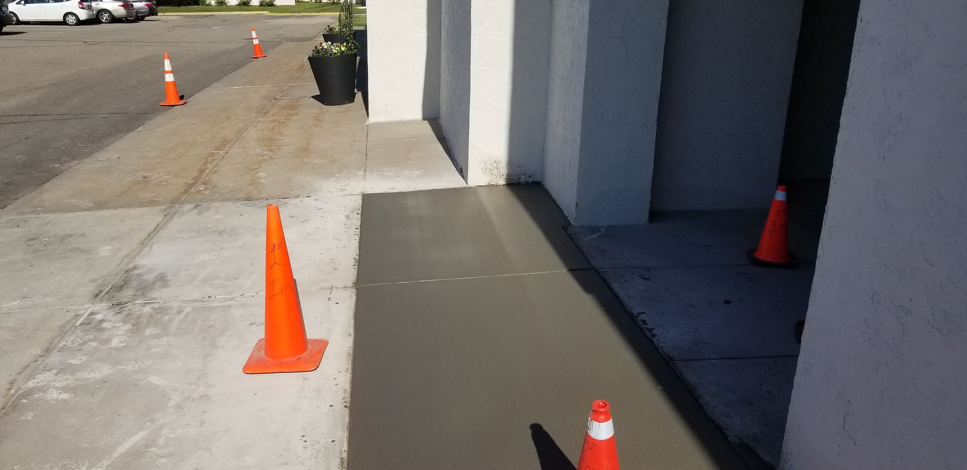 Freshly poured concrete sidewalk section, marked with orange traffic cones.