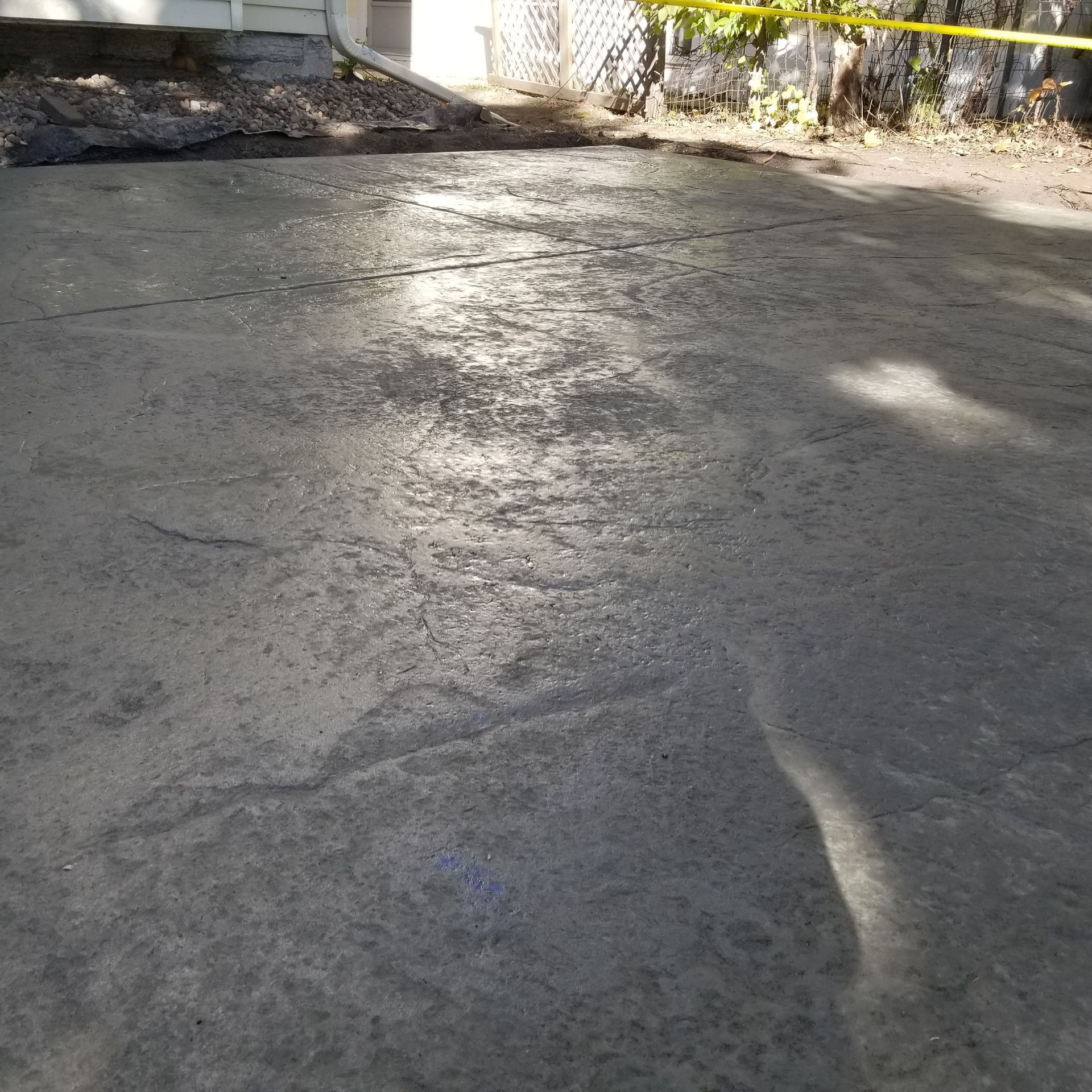 Gray, cracked asphalt driveway with sunlight reflecting off of it. Yellow caution tape is visible in the background.