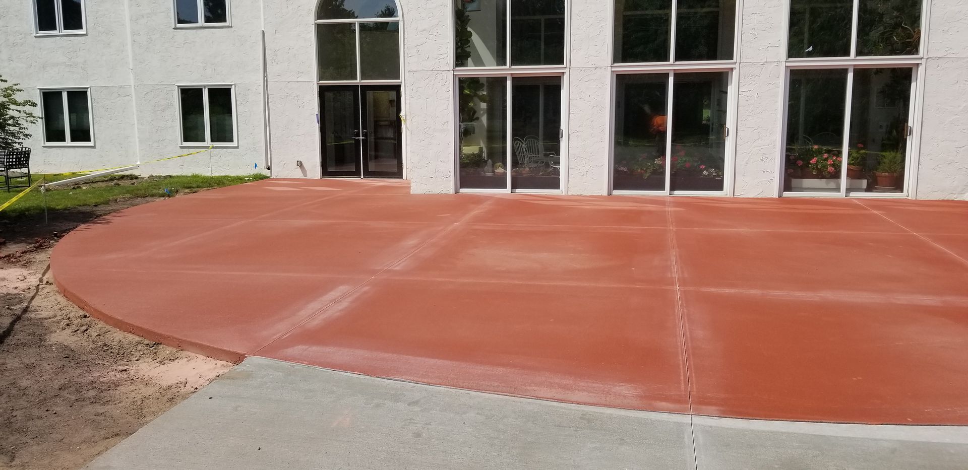 A red concrete patio in front of a building with large glass doors.