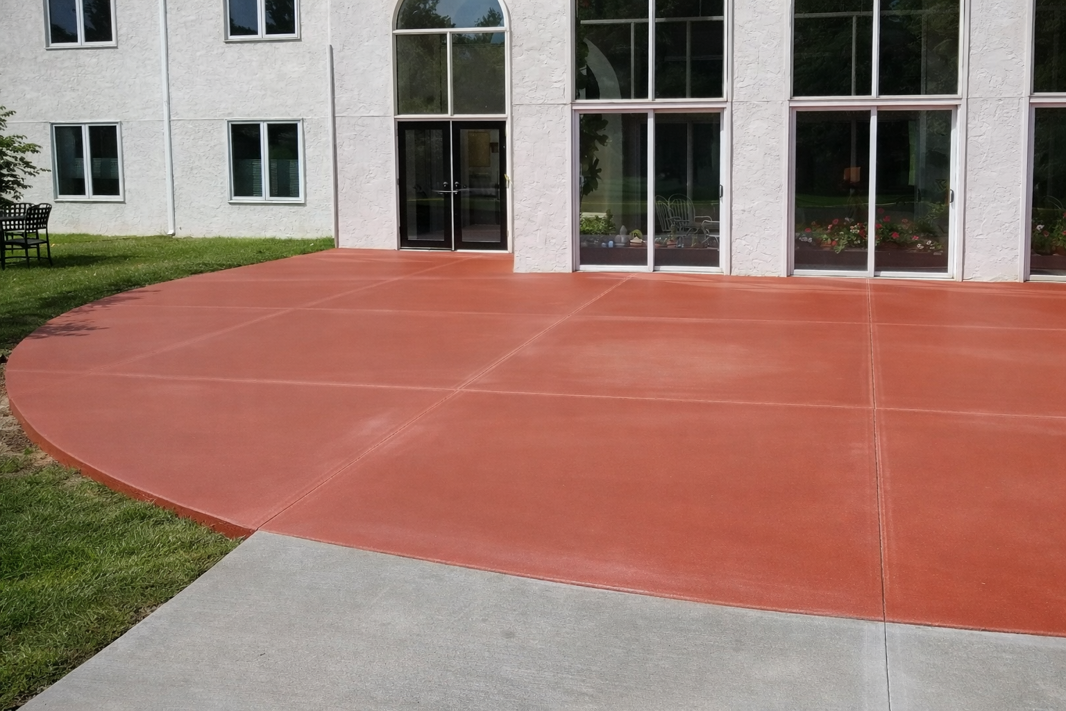 Red concrete patio in front of a building with large windows and a glass door.