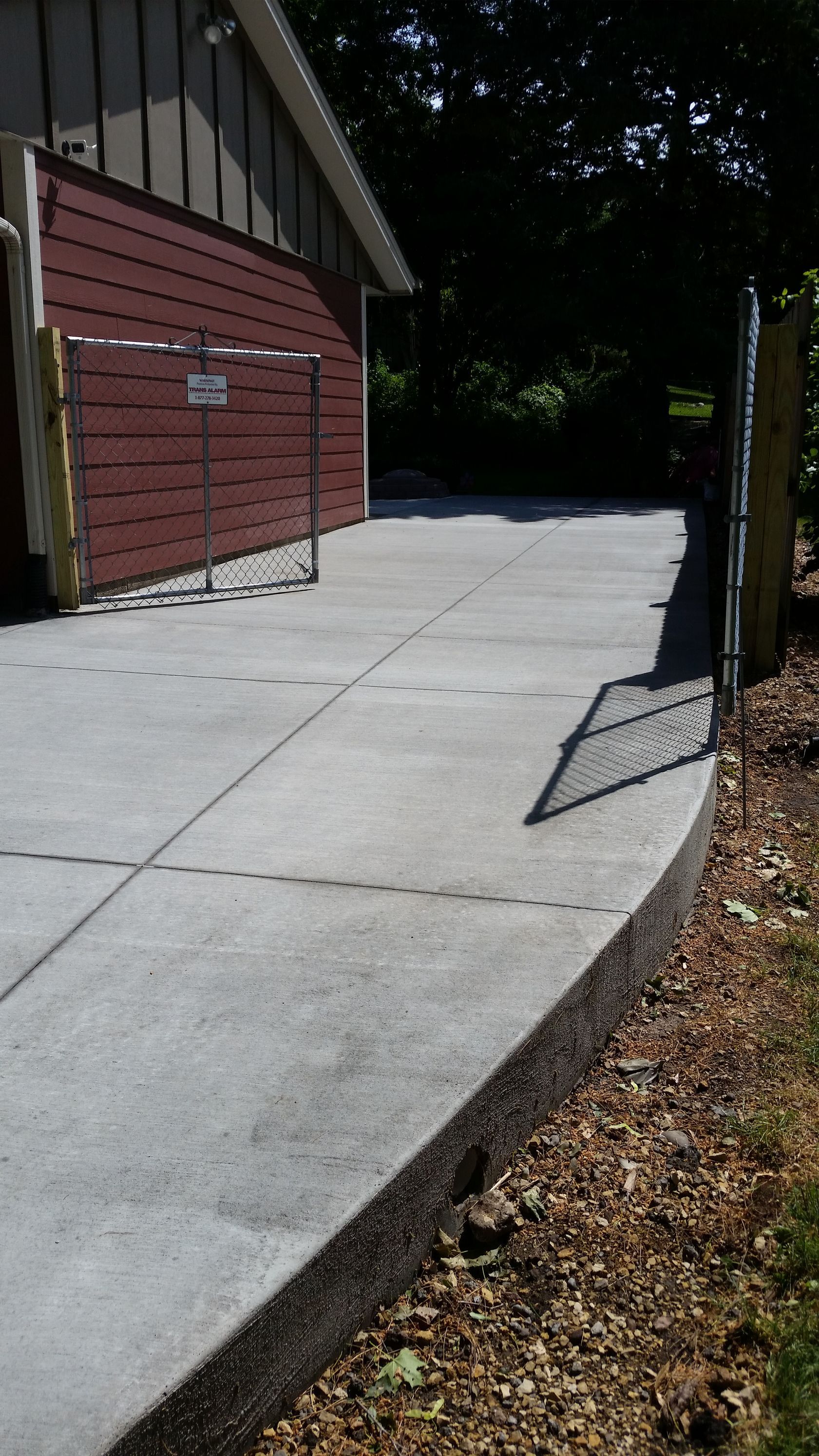 Concrete patio with a retaining wall and chain-link fence, next to a building with red siding.