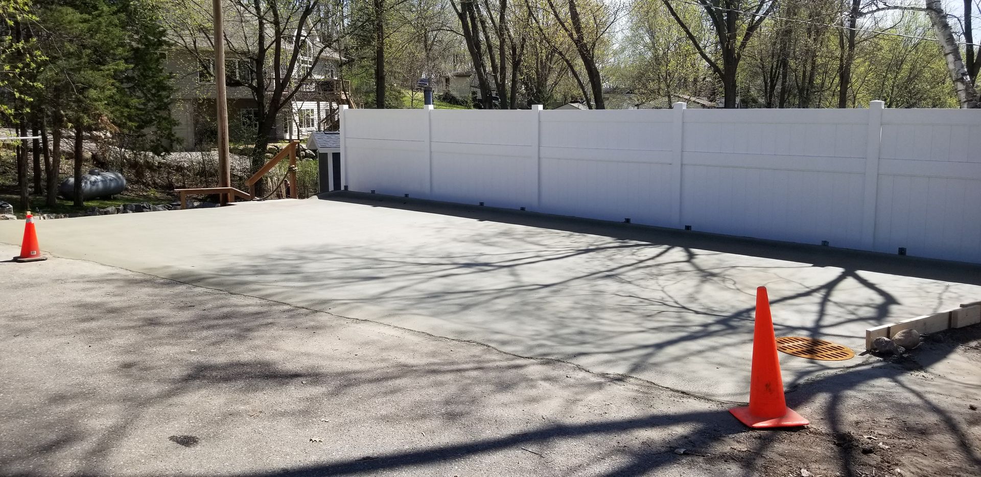 Concrete lot with orange traffic cones, next to a white wall and trees.