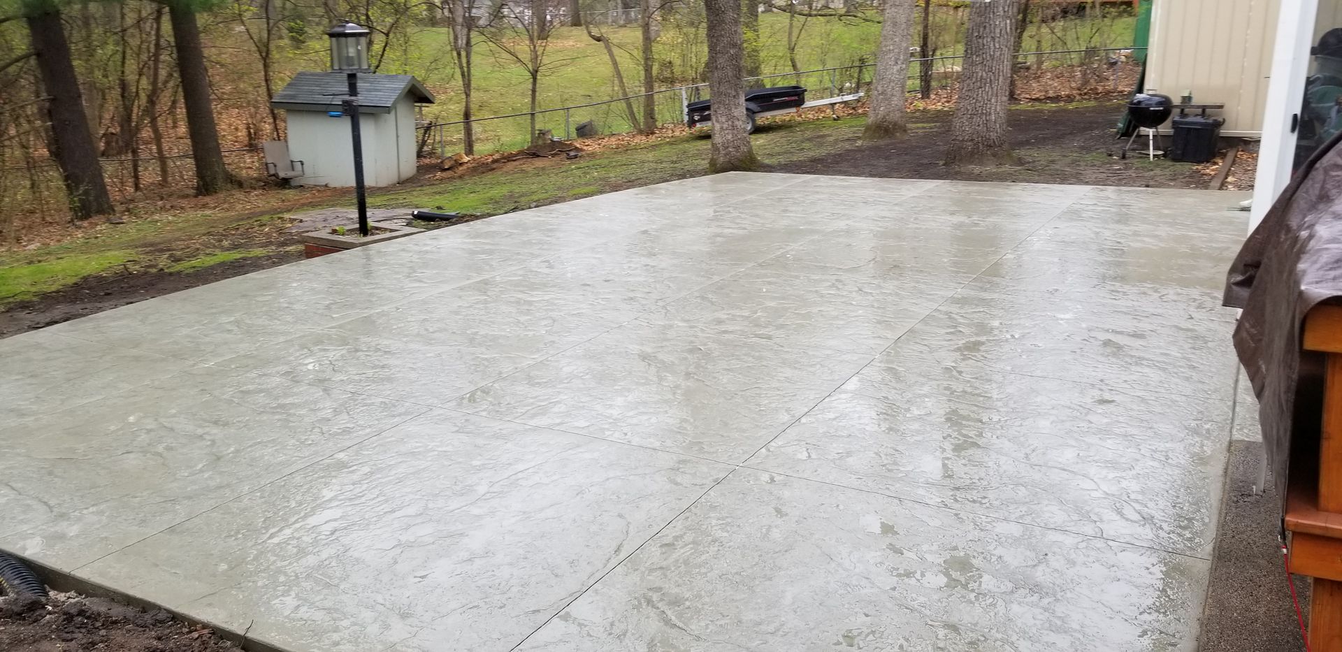 Concrete patio in a backyard with trees and a small structure.