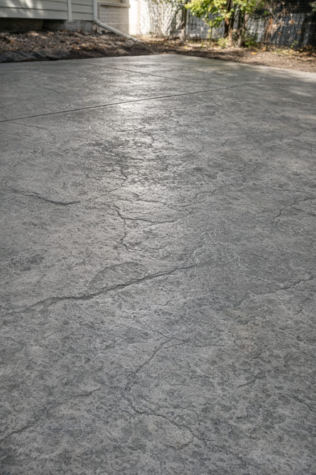 Gray, textured concrete driveway with natural cracks, outdoors.