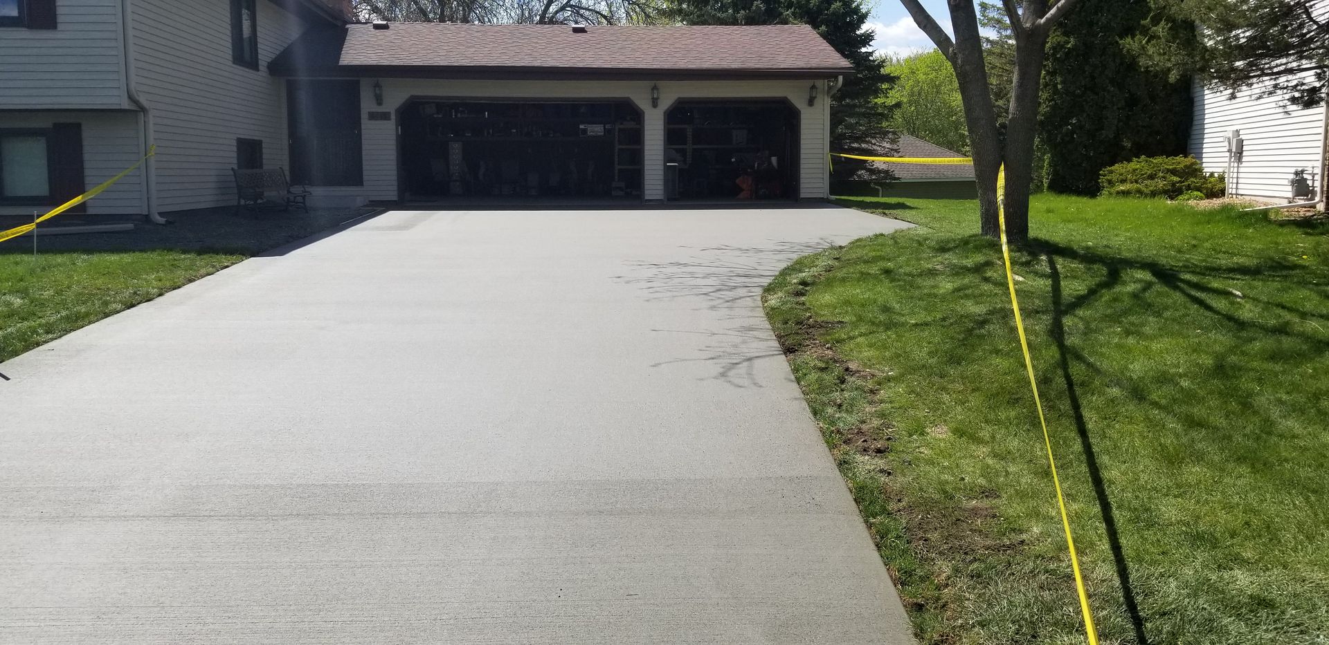 A newly paved gray driveway leads to a two-car garage. Yellow caution tape is present.